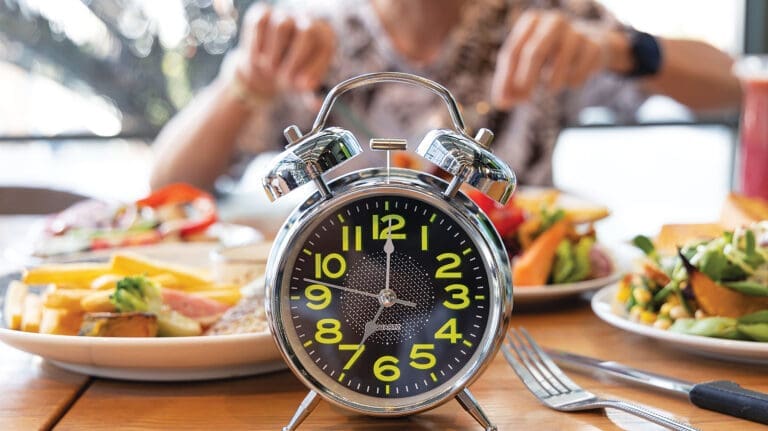 Selective Focus Of Alarm Clock With Young Man Eating A Healthy Food As Intermittent Fasting, Time Restricted Eating Diet Breakfast Image