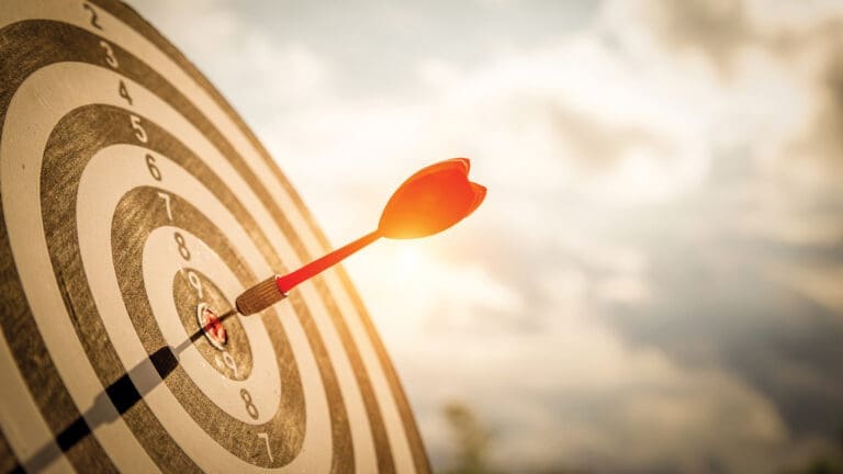 Close Up Shot Red Darts Arrows In The Target Of Dartboard Center On Dark Blue Sky Background. Business Target Or Goal Success And Winner Concept.